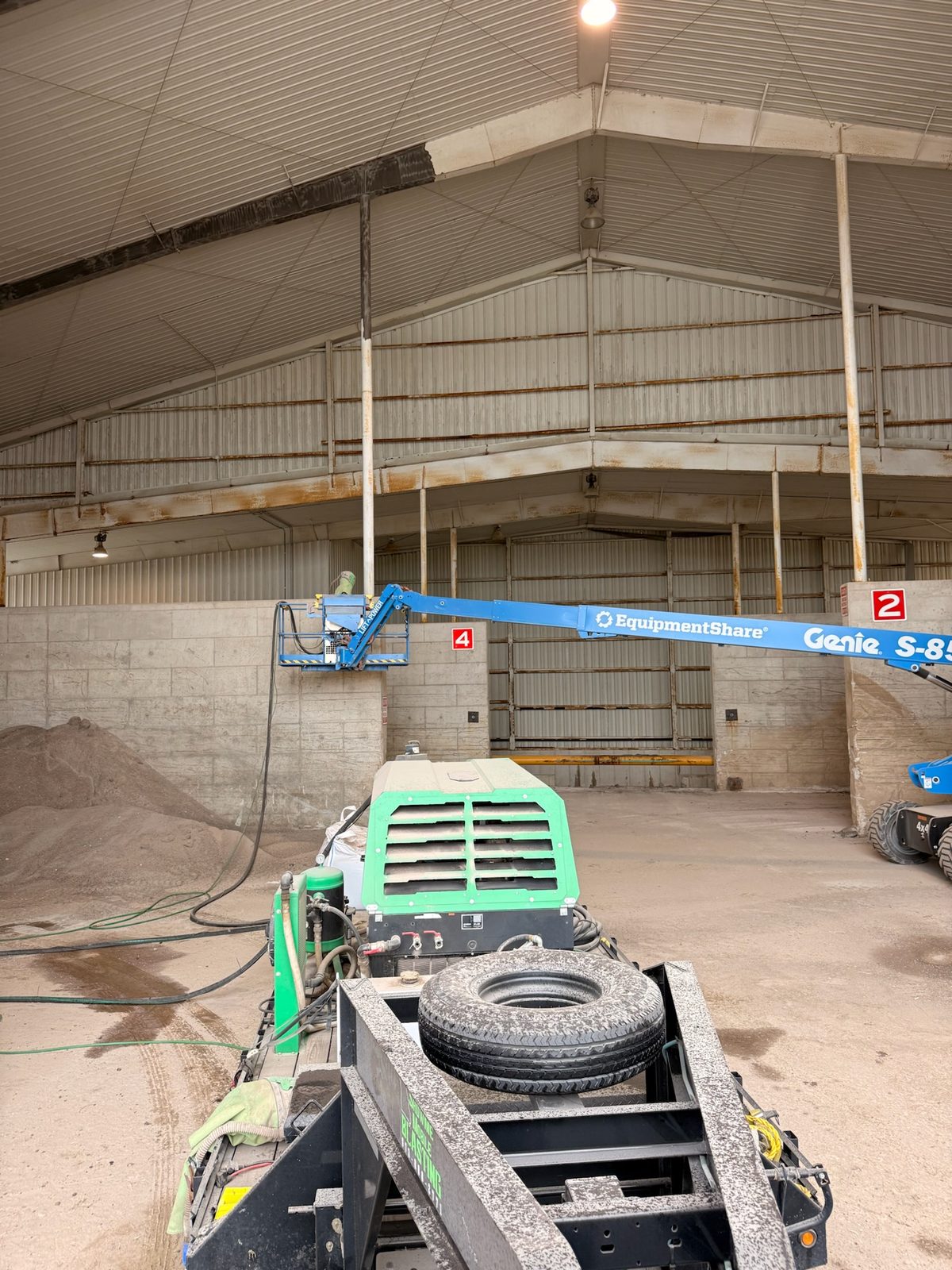 Boom lift and blasting rig staged inside a salt storage barn for structural steel cleaning